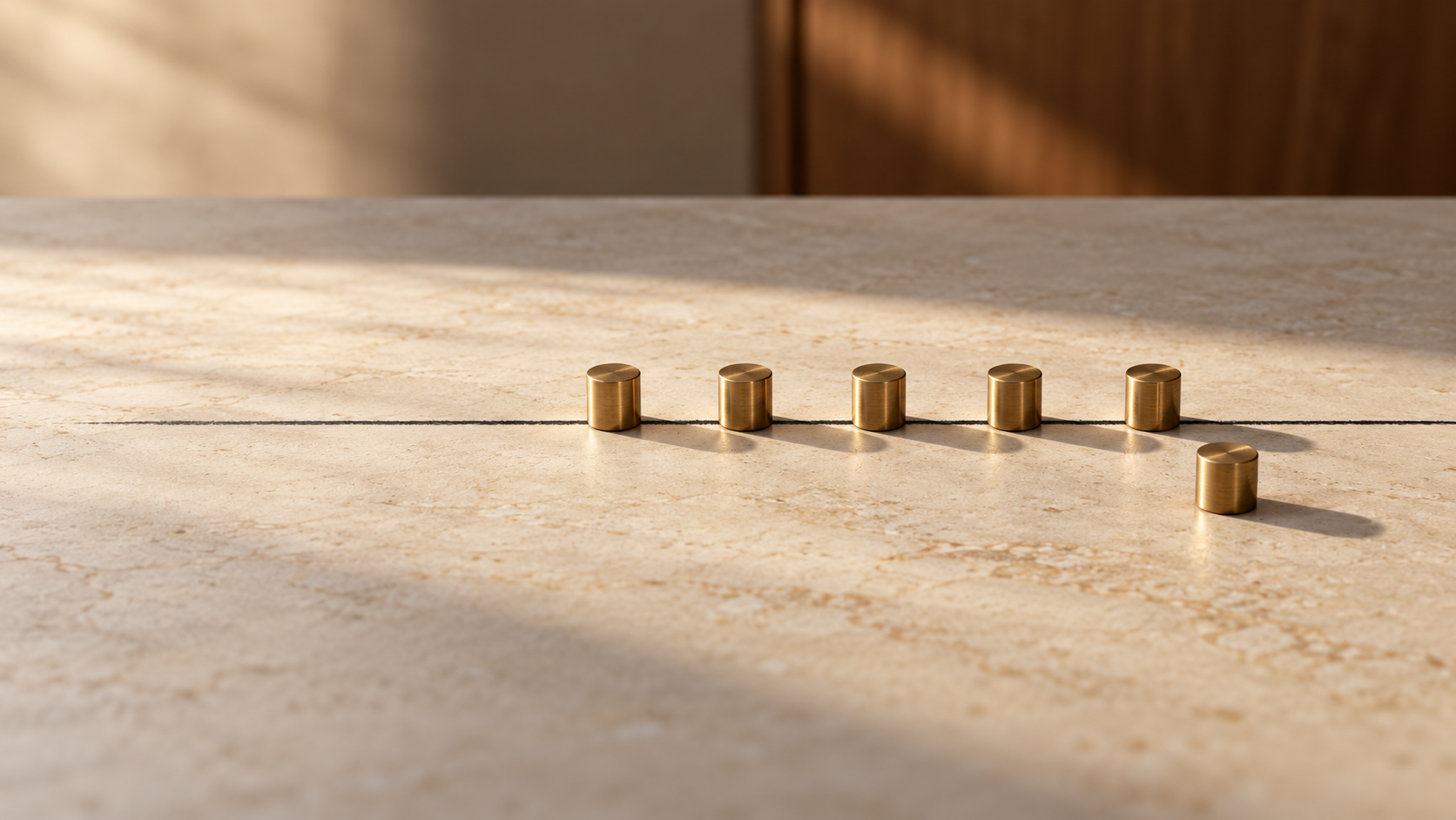 Five brass markers follow a straight line while one stands outside it on a cream stone surface.